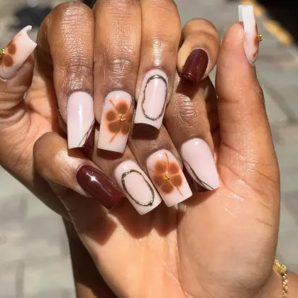 Square nude nails with painted brown flowers, gold outlines and one oxblood accent